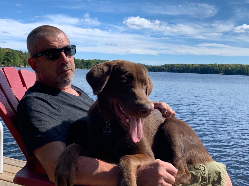 The founder of Four Paws Movers sitting lakeside with his chocolate Labrador, Ranger